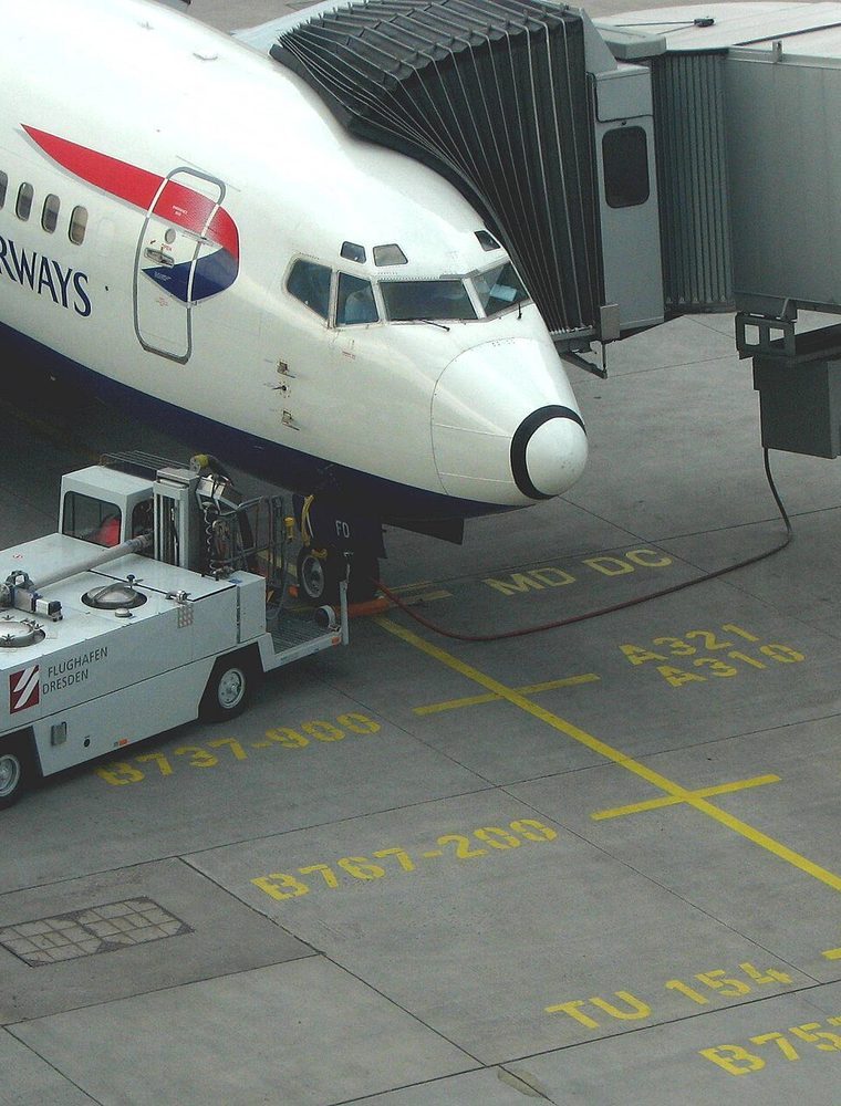 An airliner docked at a jet bridge with ground handling equipment on the apron.