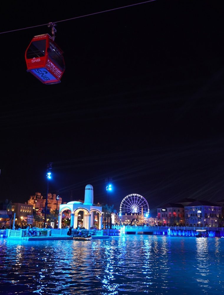 Riyadh waterfront at night, illuminated in blue with a cable car overhead.